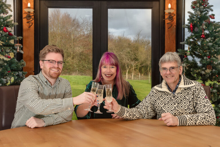 Three people toasting with champagne by Christmas tree.