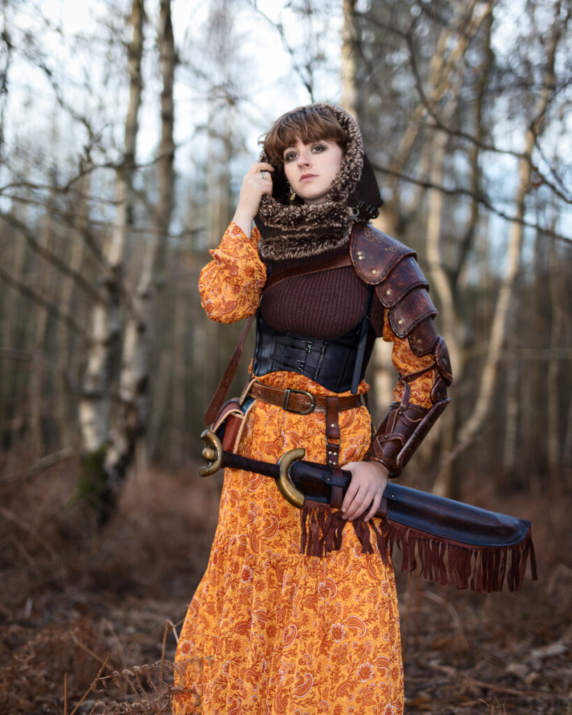 Woman in medieval armour with sword in forest.