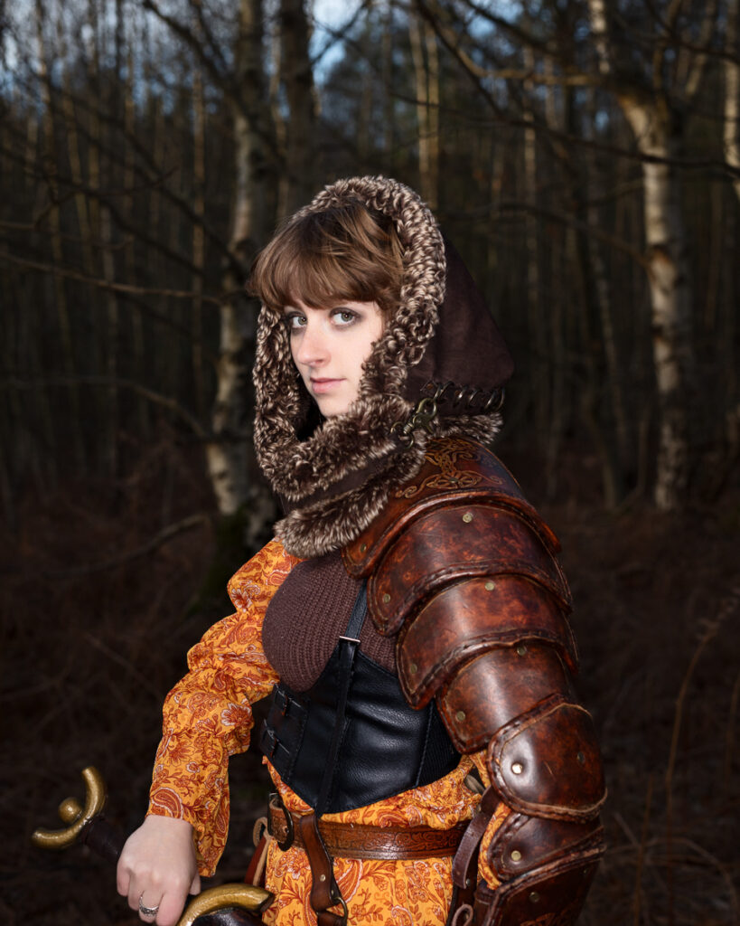 Woman in medieval costume with fur hood in forest.