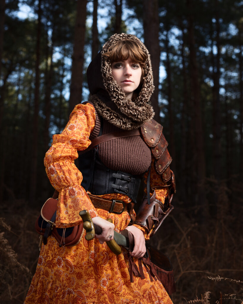 Woman in medieval costume with sword in forest.