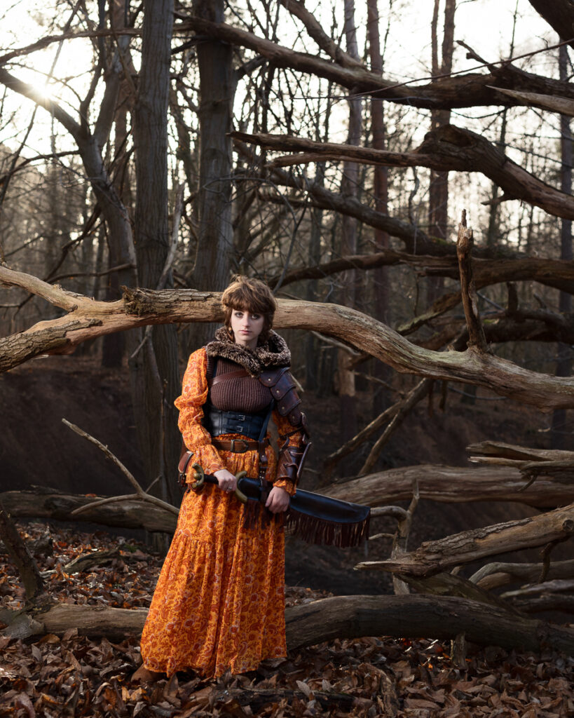 Woman in medieval dress holding a sword in forest.