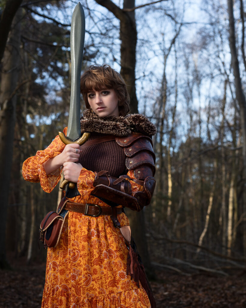 Woman in medieval armour with a sword in forest.