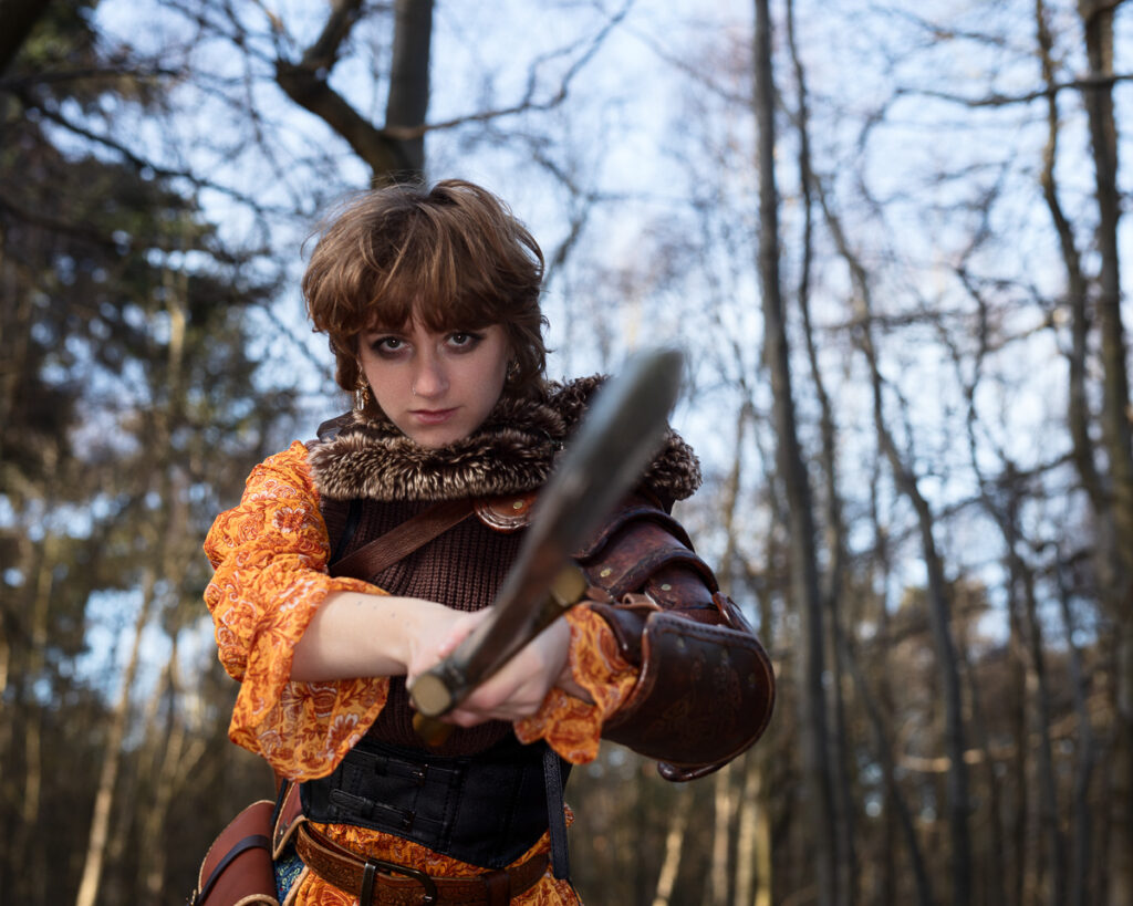 Person in medieval costume with sword in forest.