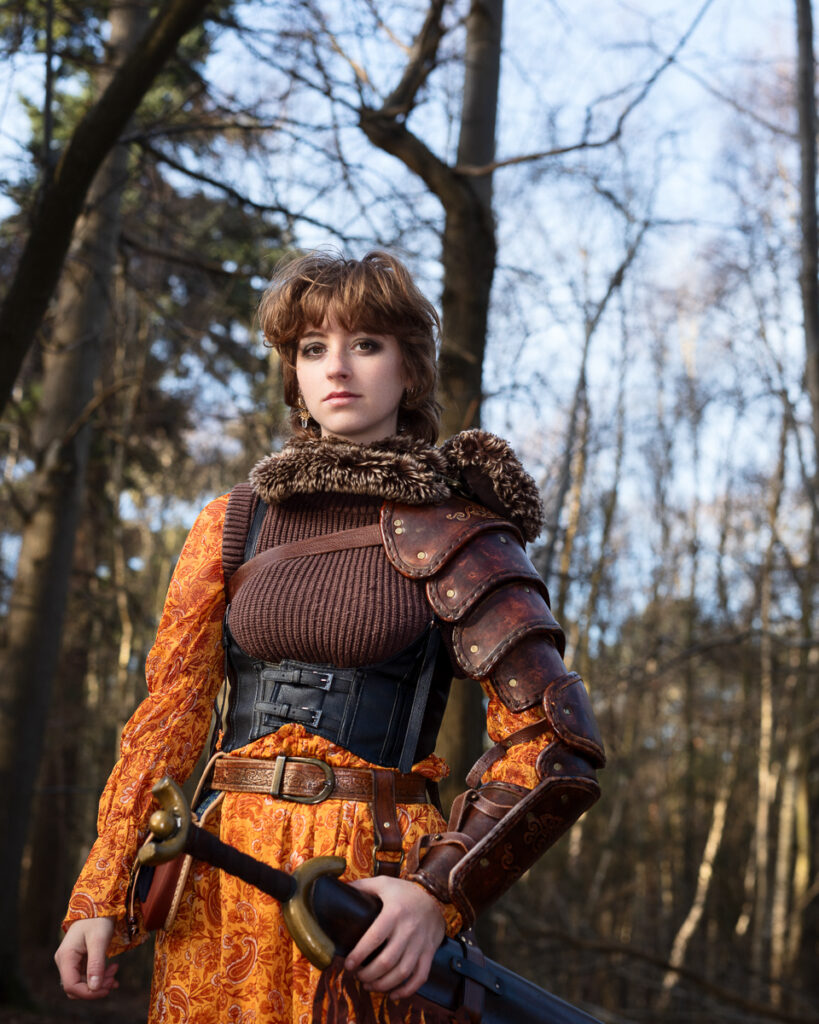 Woman in medieval armour holding a sword in forest.