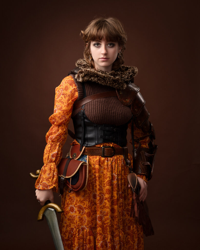 Woman in medieval costume holding sword, brown background.