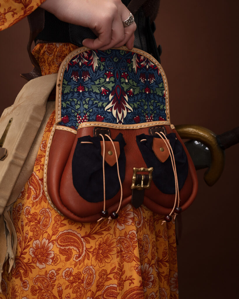 Hand holding a floral tapestry leather bag.