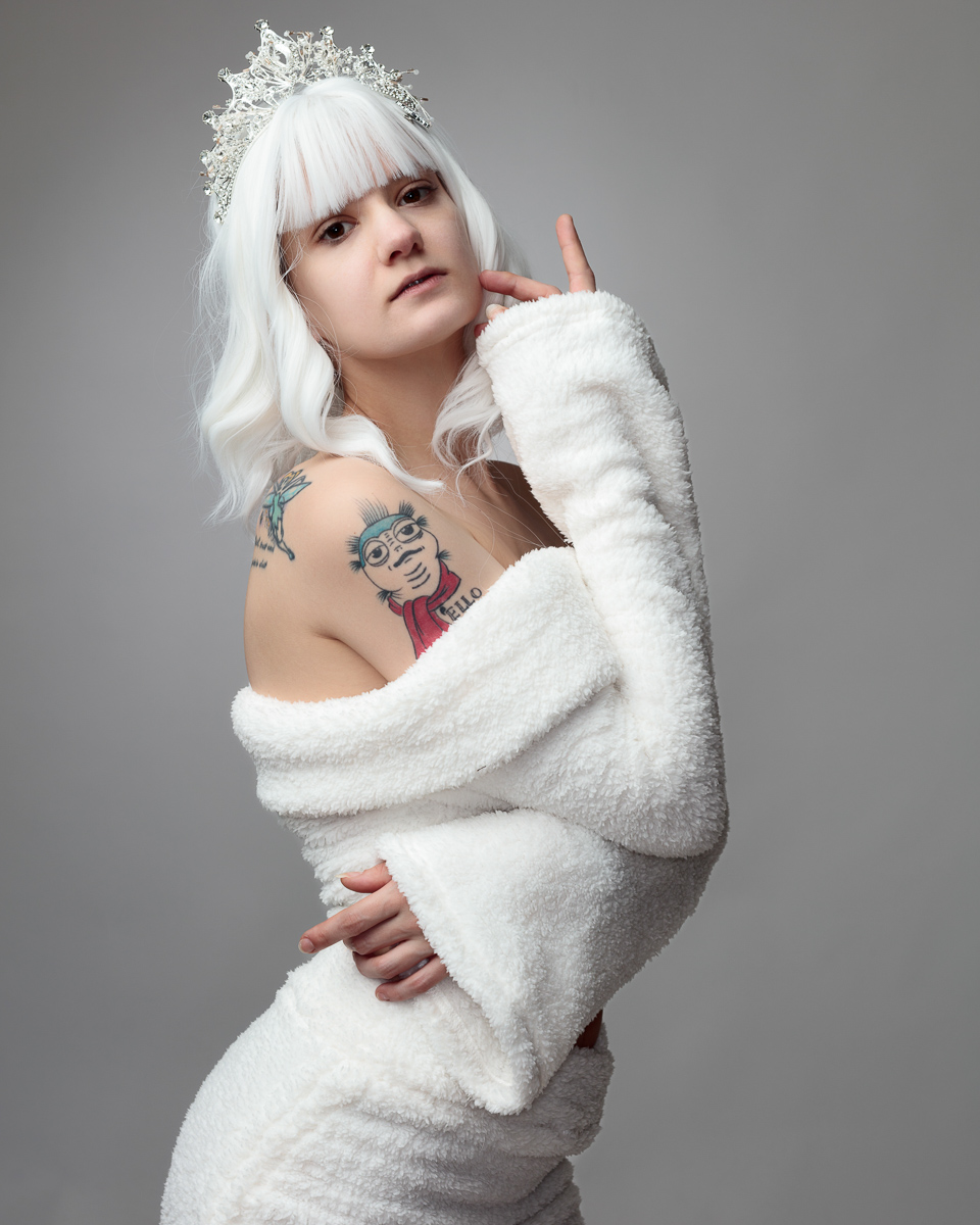 Woman in white robe and crown, arm tattoo visible.