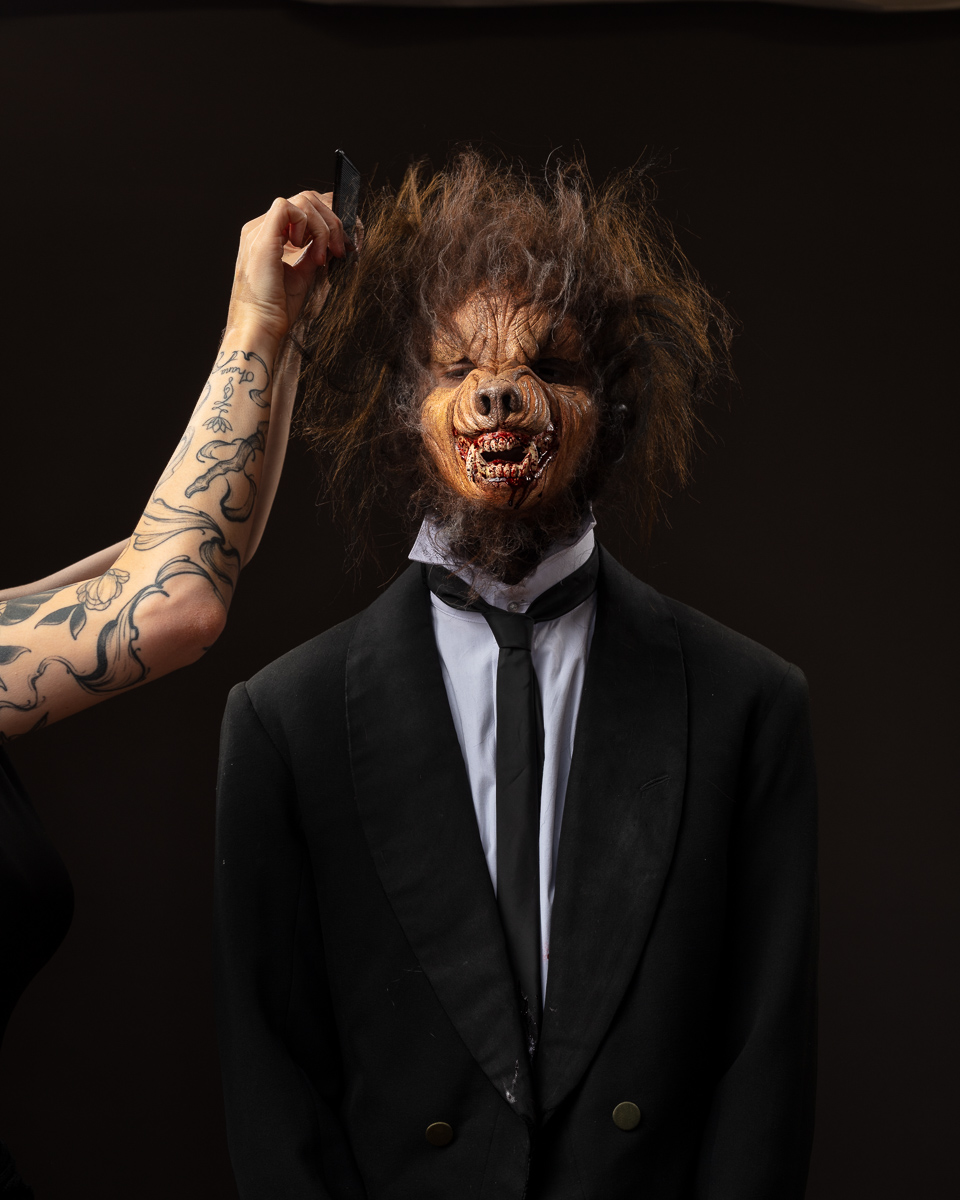 Person in a werewolf mask getting hair styled.