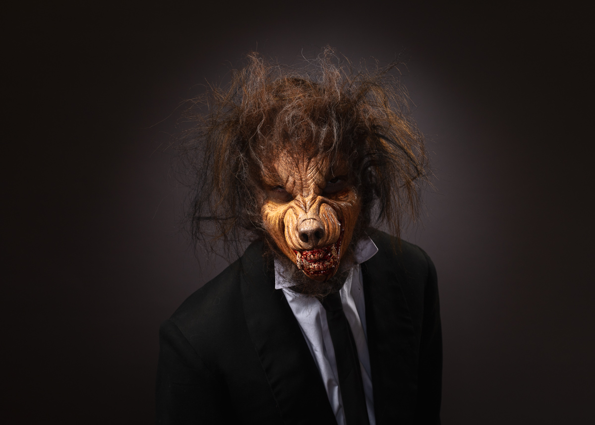 Person in werewolf costume and suit, dark background.