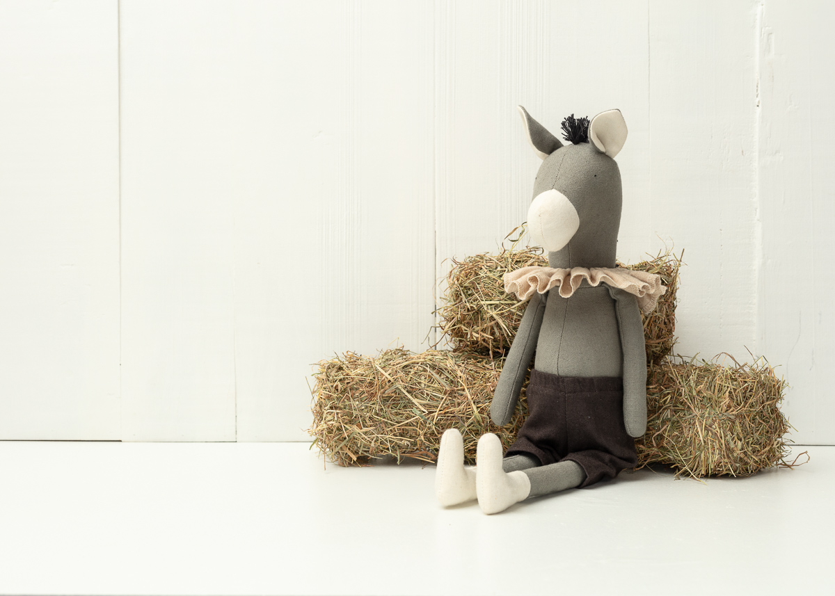 Stuffed toy horse sitting on hay bales.
