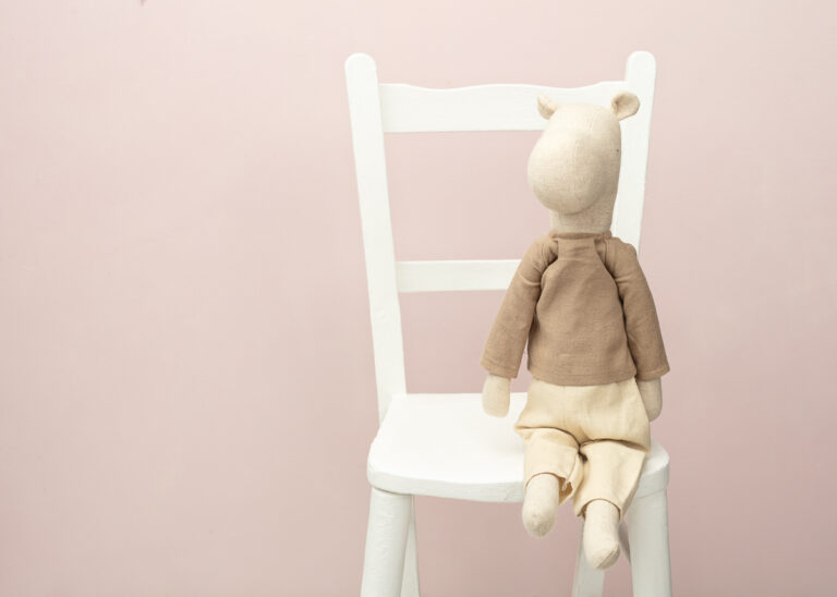 Stuffed animal on white chair against pink background.