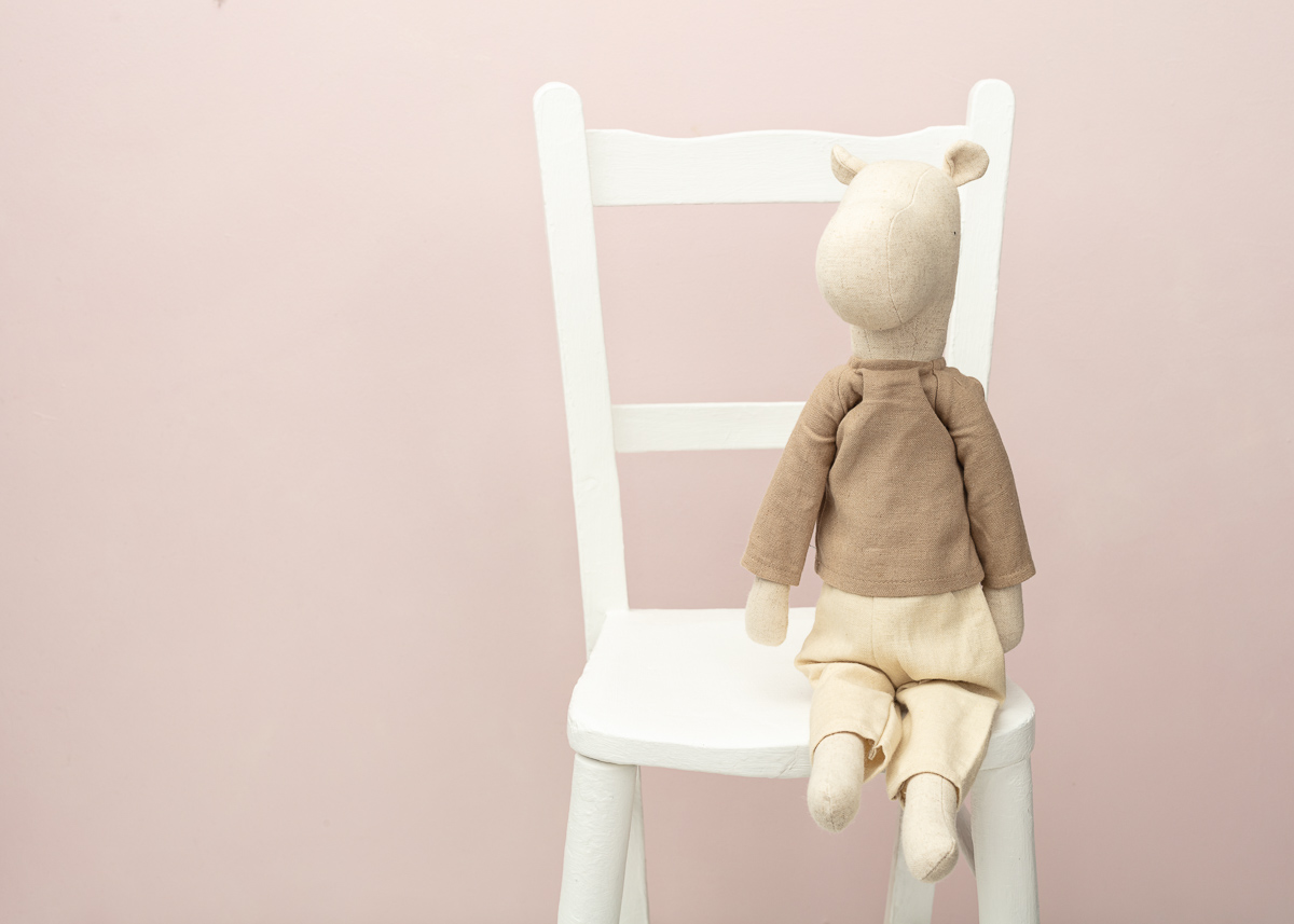 Stuffed animal on white chair against pink background.