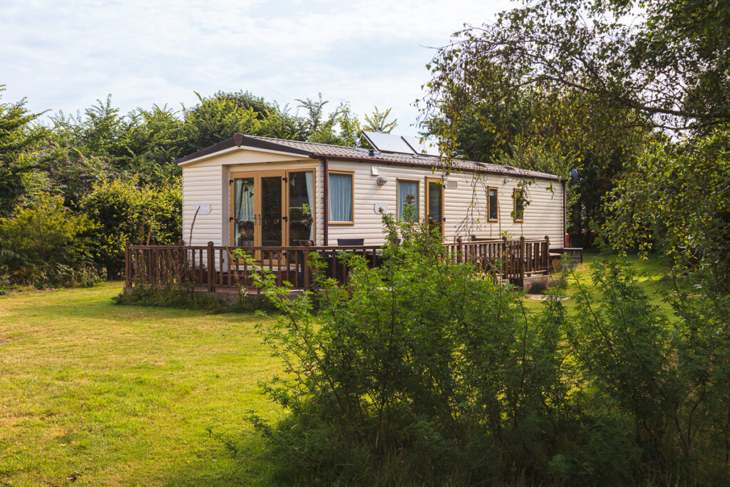 Static caravan with a timber deck among green trees on a holiday estate at Dunwich