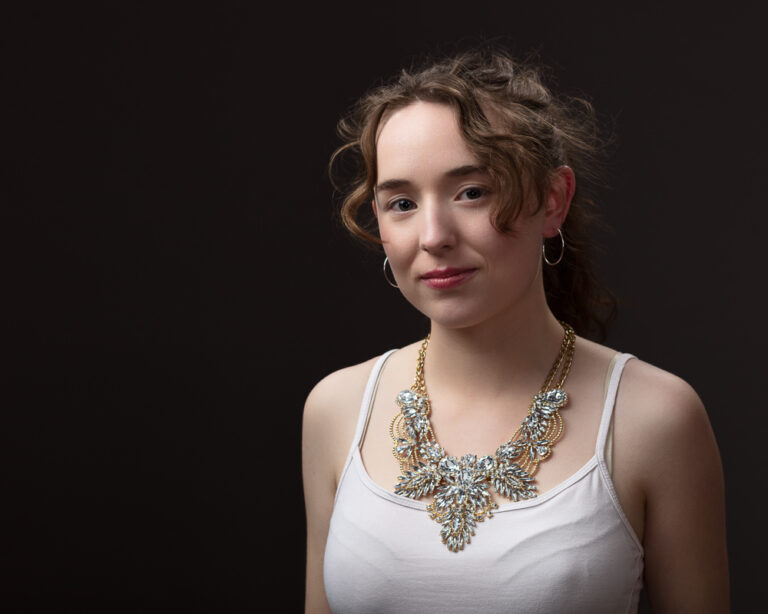 Woman wearing ornate necklace against dark background.