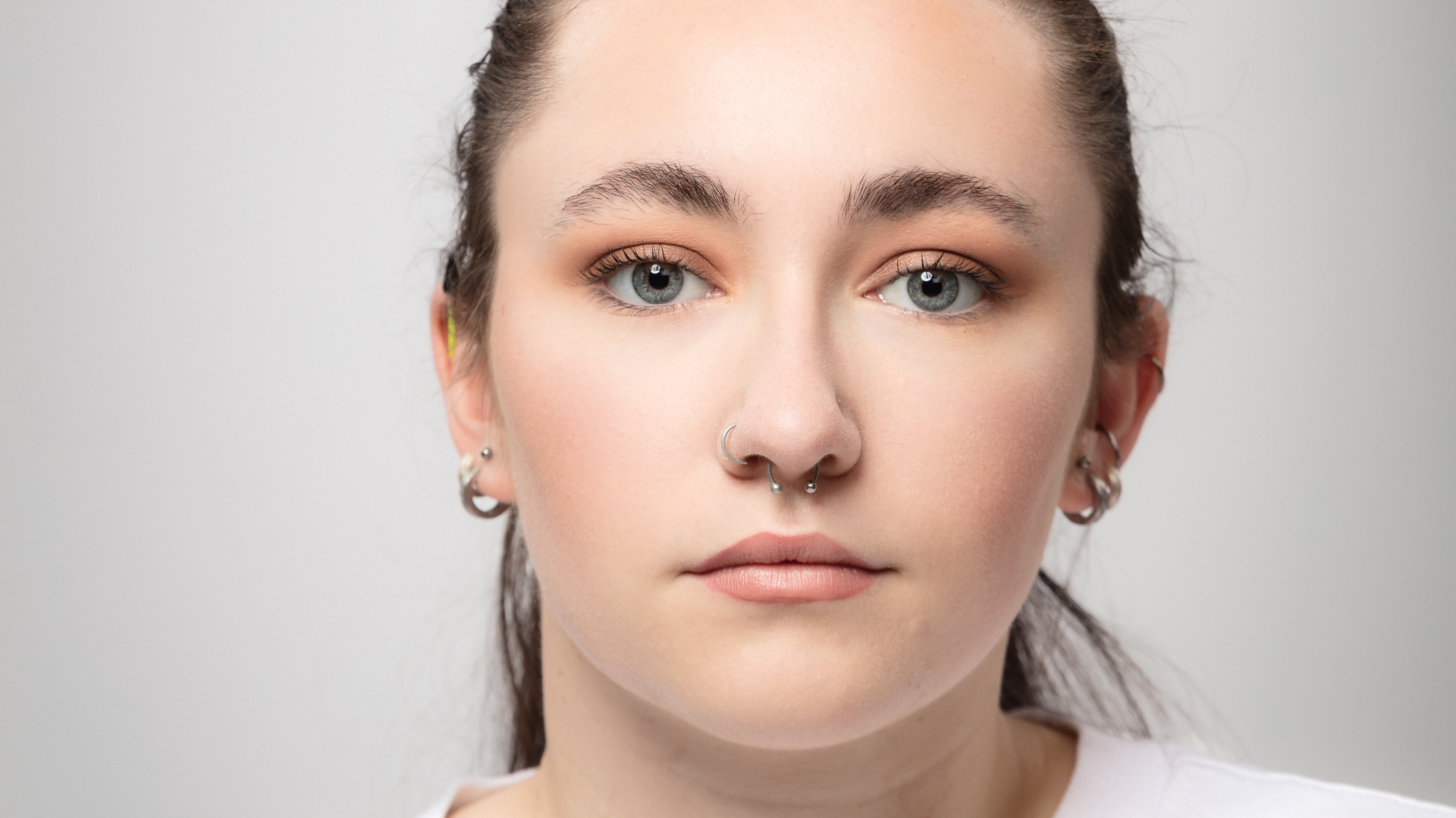 Close-up actor headshot of a young woman with her hair tied back, against a light grey background