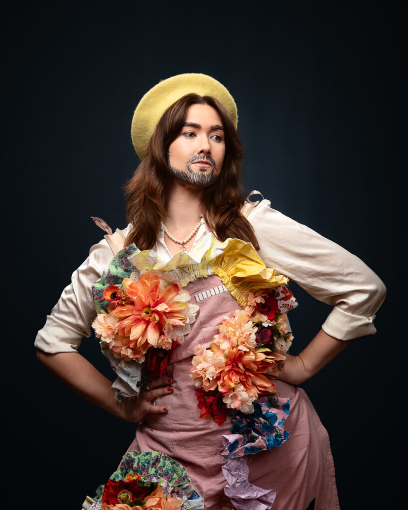 Person in colourful floral outfit with beard-like makeup.
