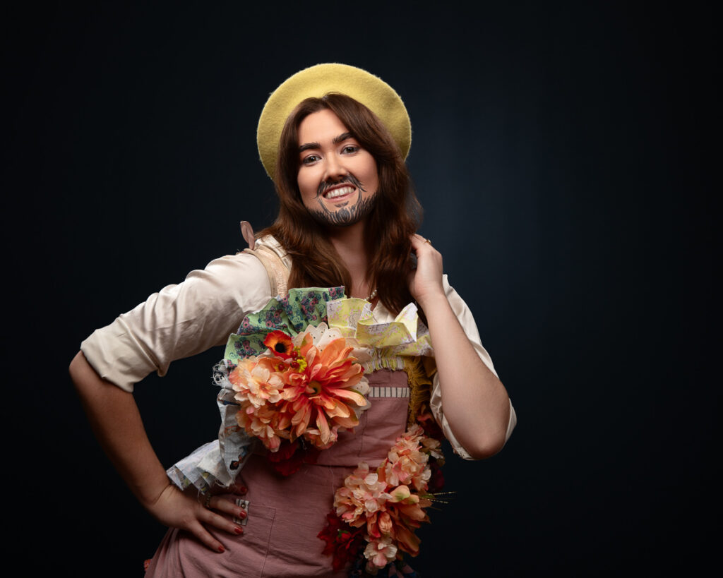 Person with beard wearing flower-decorated outfit and hat.