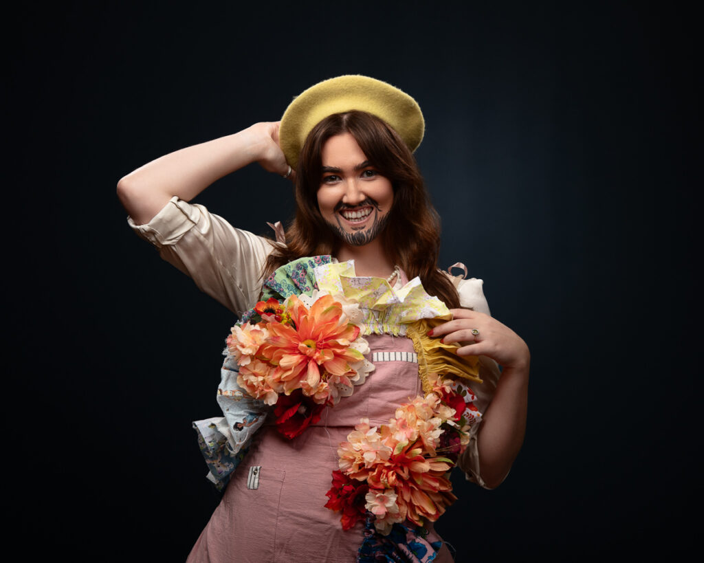 Person with painted beard, wearing floral accessory and beret.