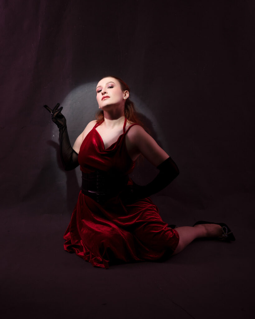 Woman in elegant red dress poses on dark background.