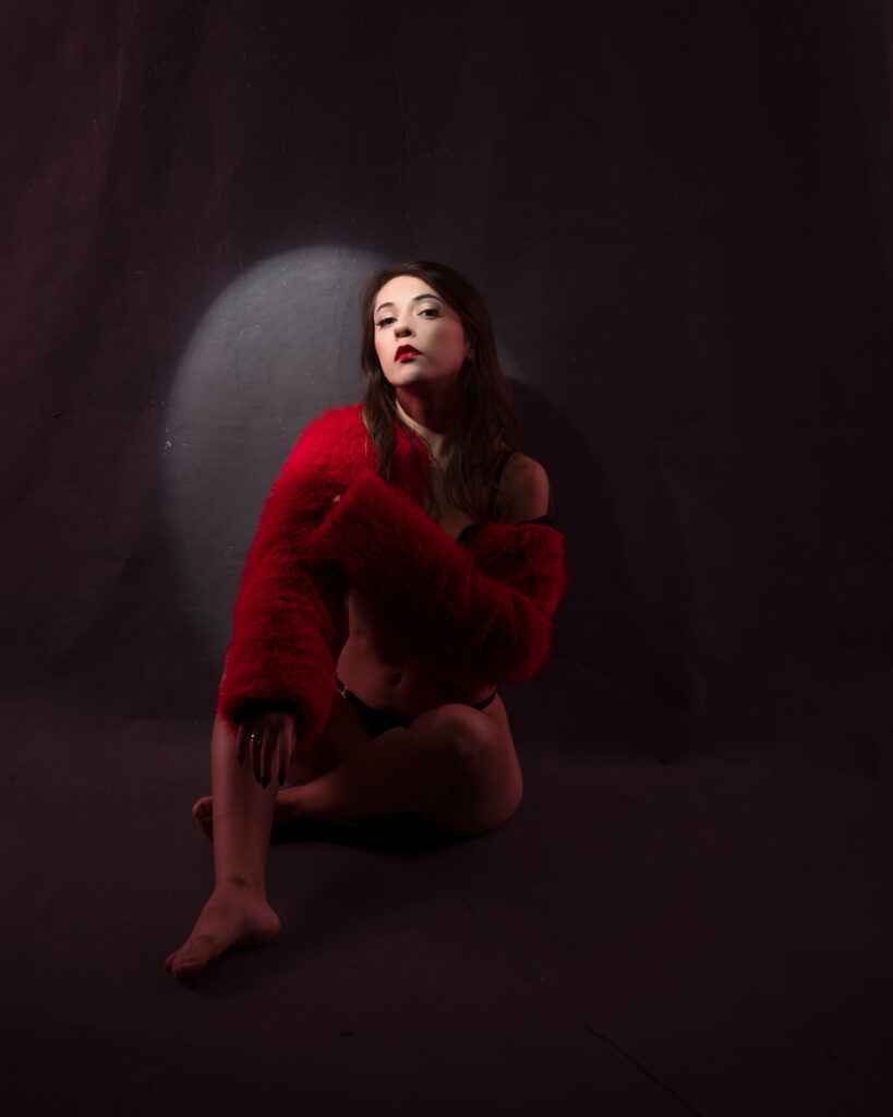 Woman in red coat posing on dark background.