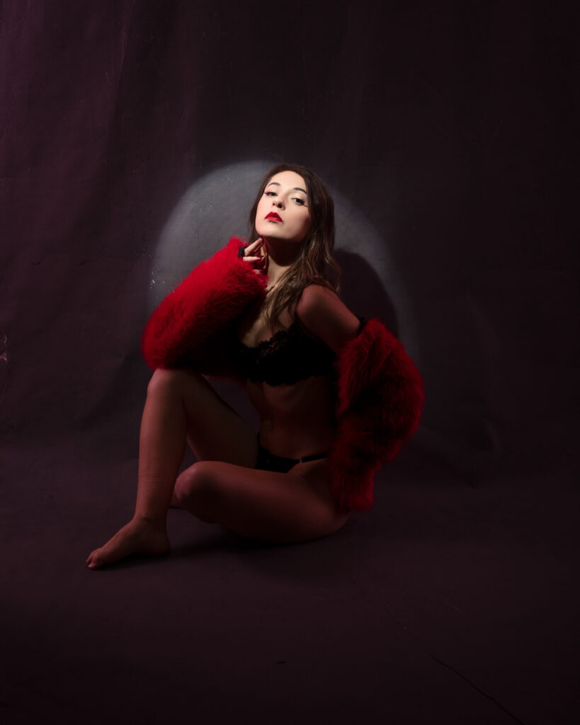 Woman in red fur coat posing on dark background.