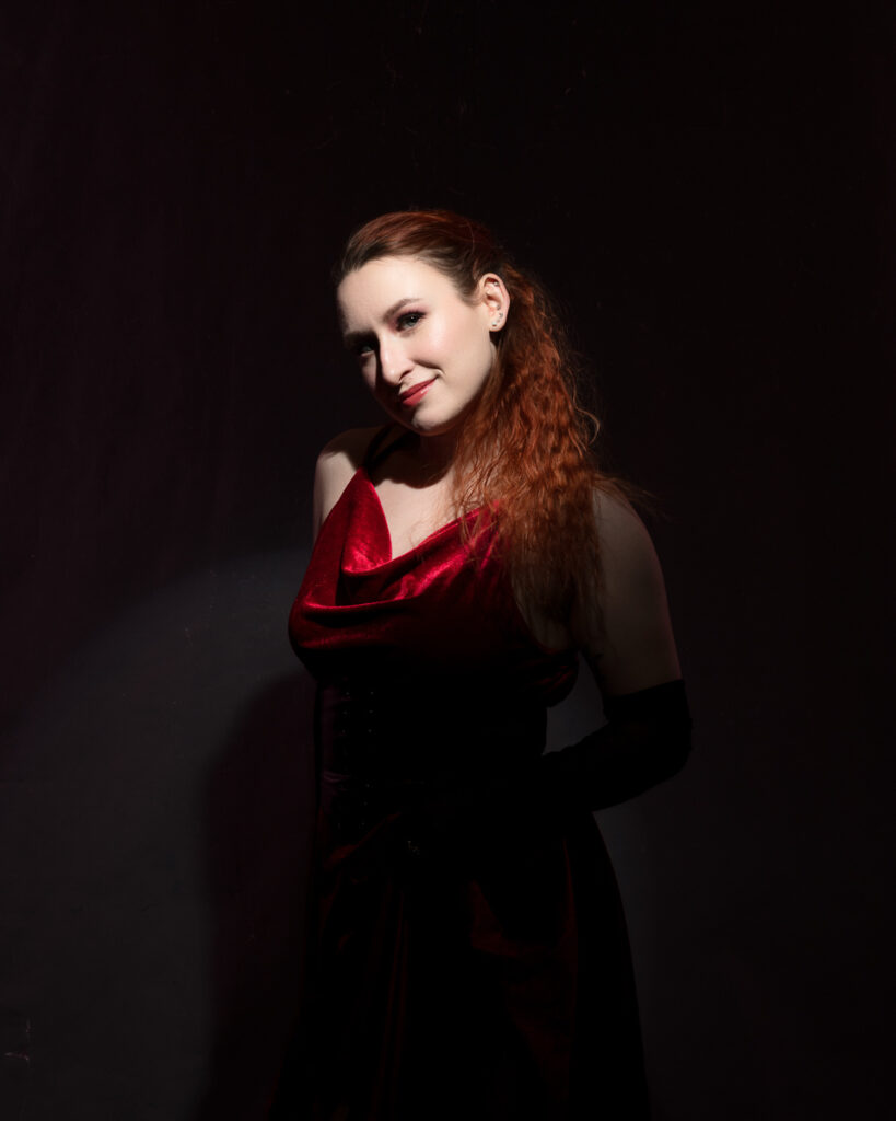 Woman in elegant red dress posing in darkness.