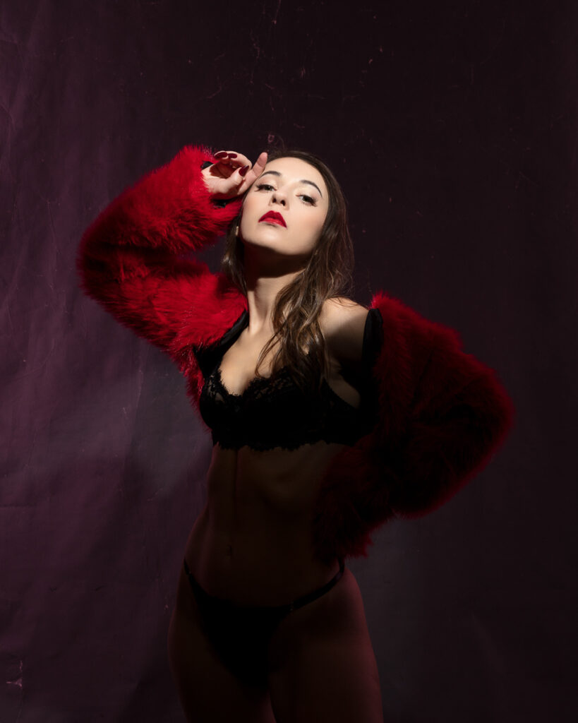 Woman in red fur jacket and black lingerie posing.