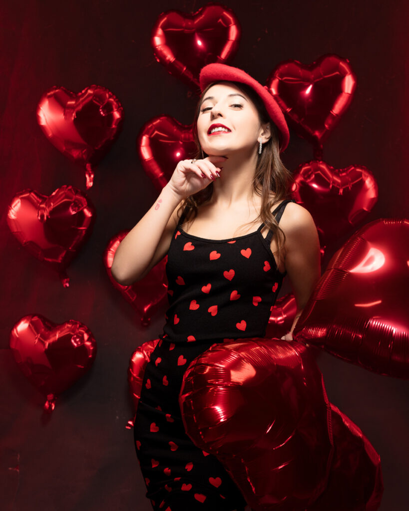 Woman in heart-patterned dress with red balloons.