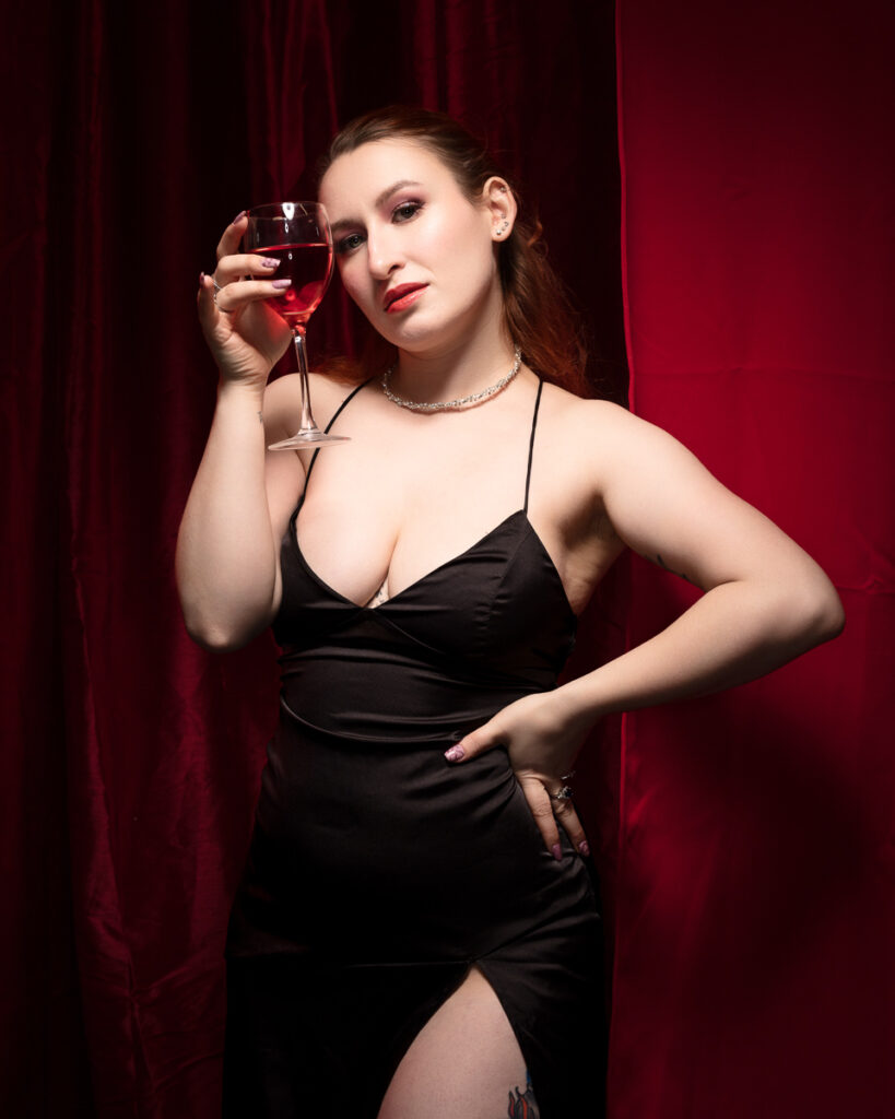 Woman in black dress holding wine glass.