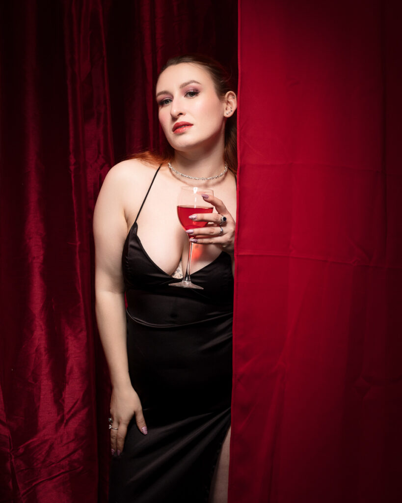 Elegant woman with drink behind red curtain.