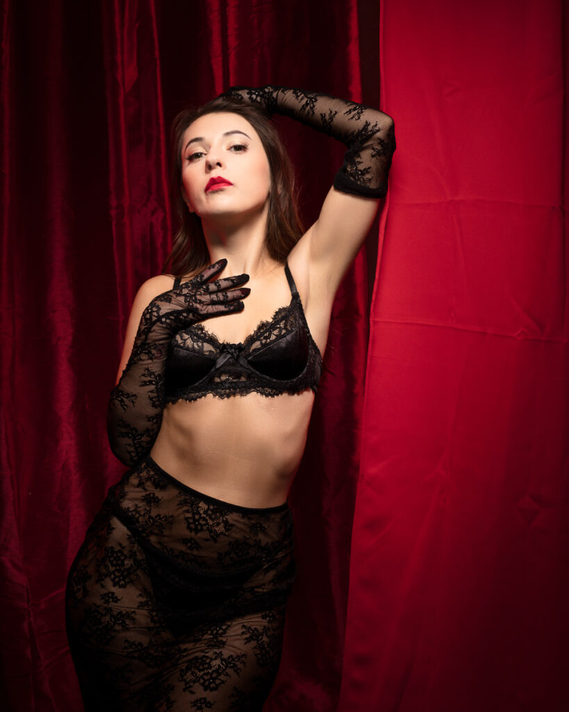 Woman in lace outfit posing against red curtain.