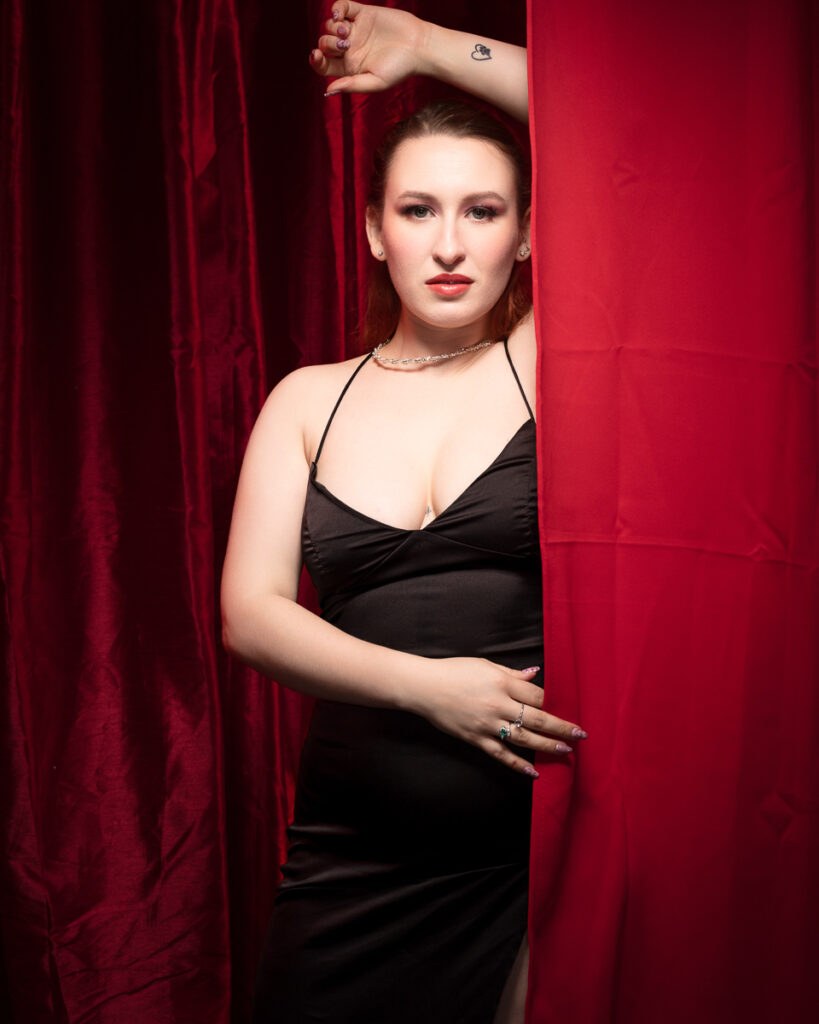 Woman in black dress with red curtain background.