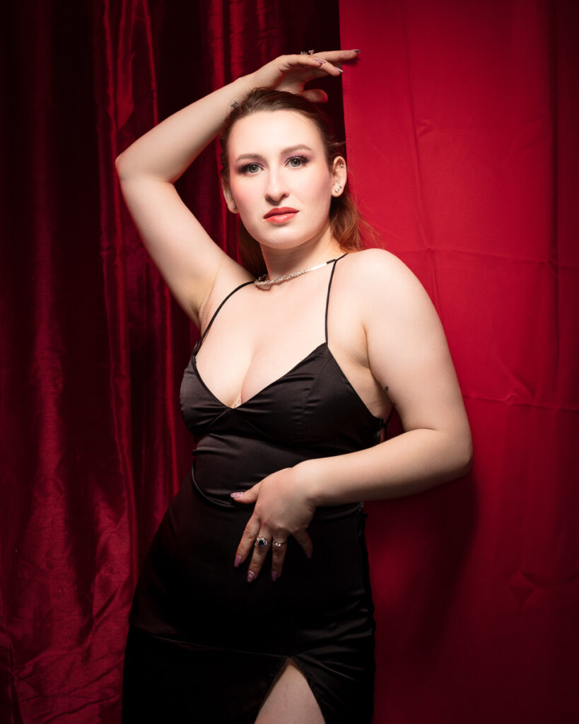 Person in black dress posing by red curtain