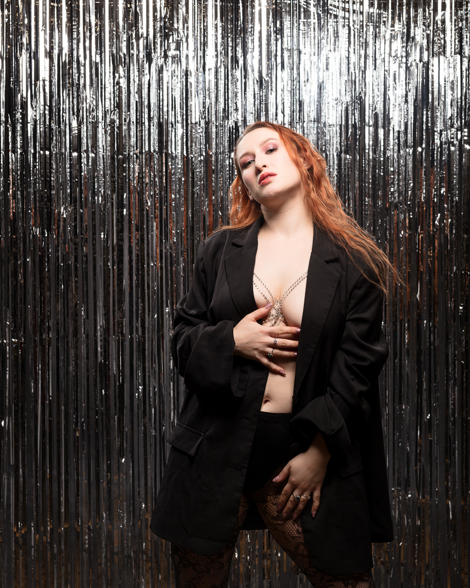 Fashionable woman in black blazer by metallic curtain.