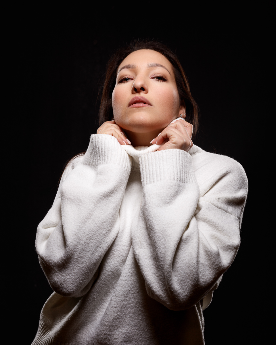Woman in white sweater posing confidently on black background.