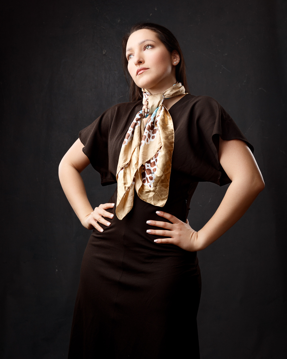 Studio portfolio portrait of Mariana in a brown vintage-style dress with a patterned scarf, hands on hips