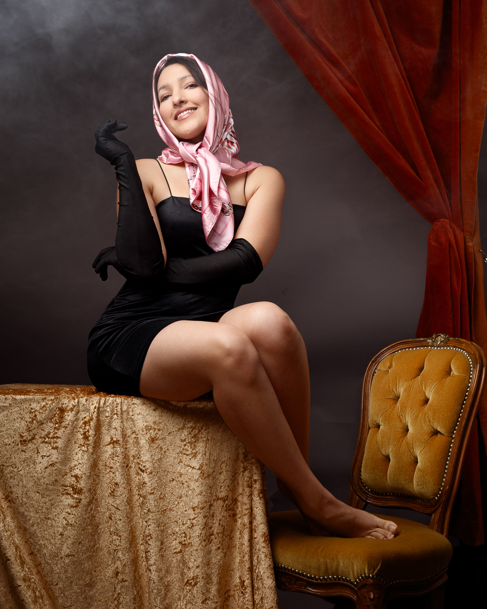 Woman in elegant outfit, seated with headscarf.
