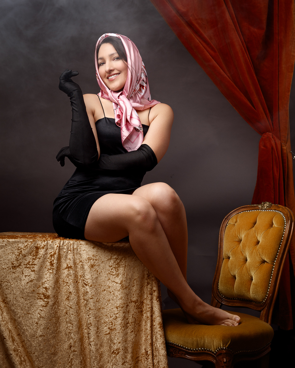 Smiling woman in vintage scarf and gloves, seated.