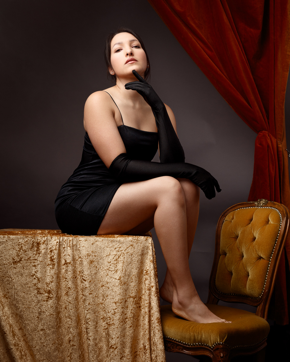 Woman in black dress posing indoors elegantly.