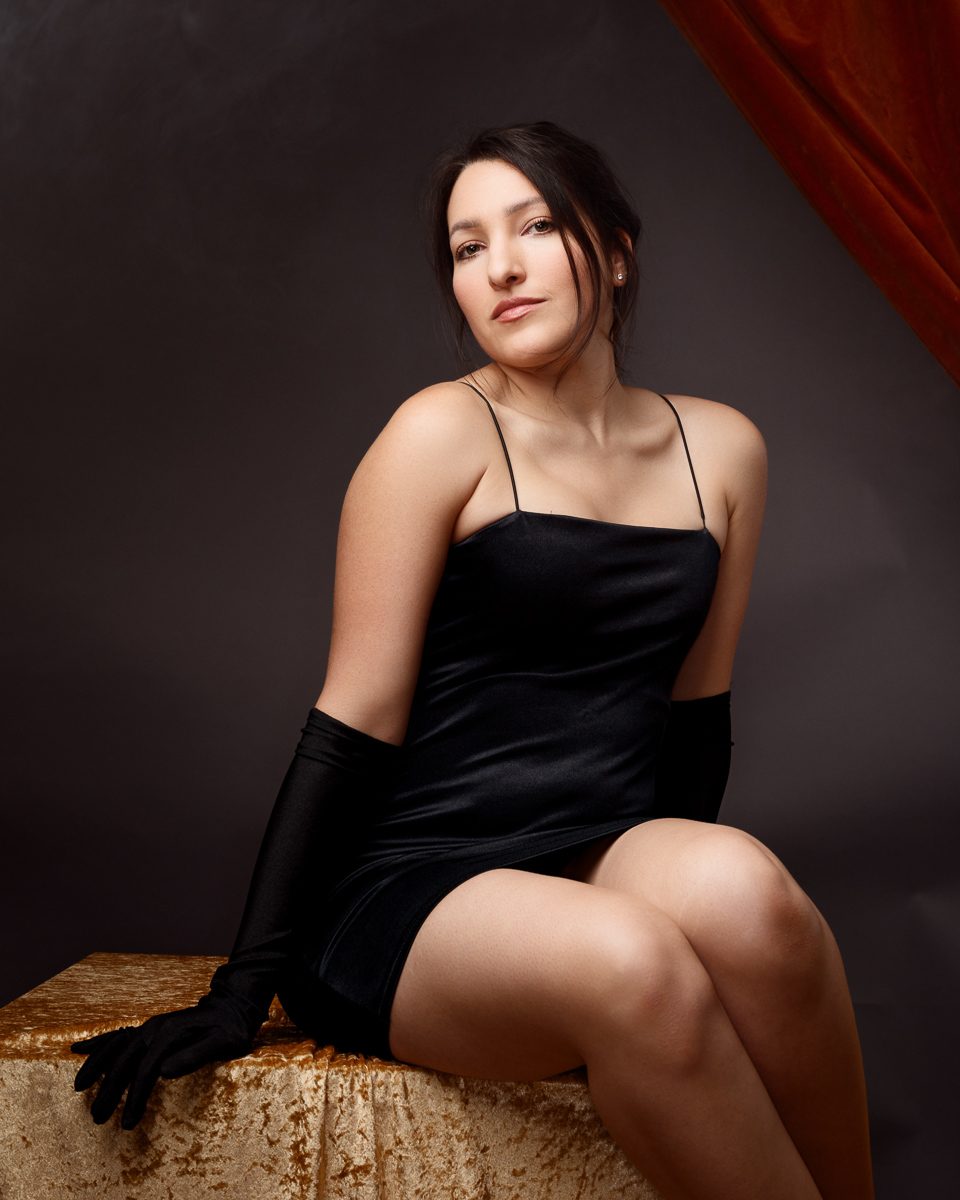 Woman in black dress posing elegantly indoors.