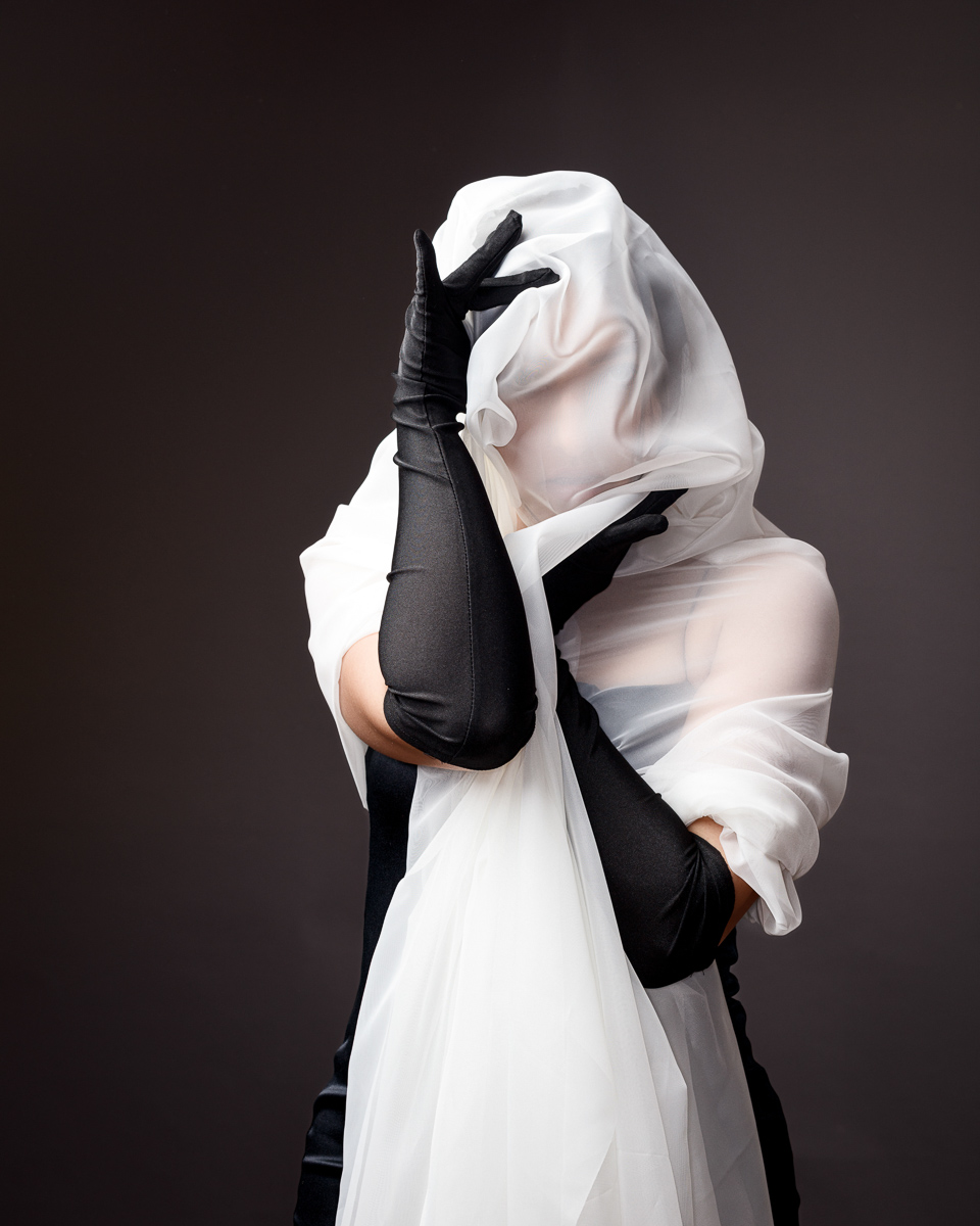 Person shrouded in sheer fabric wearing black gloves.