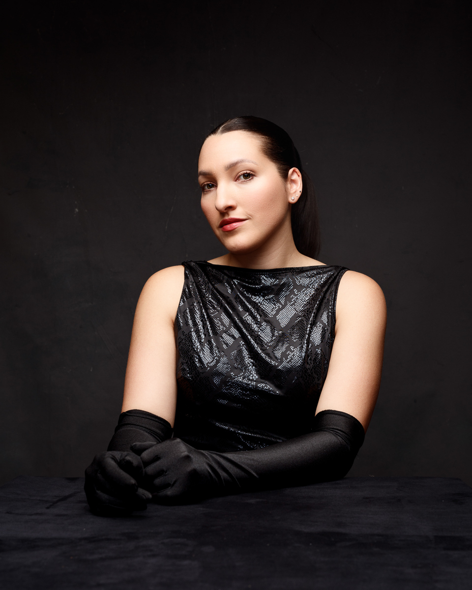 Person in elegant black outfit with gloves seated.