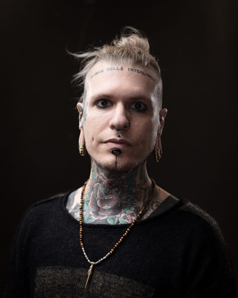 Person with tattoos and piercings facing camera solemnly.
