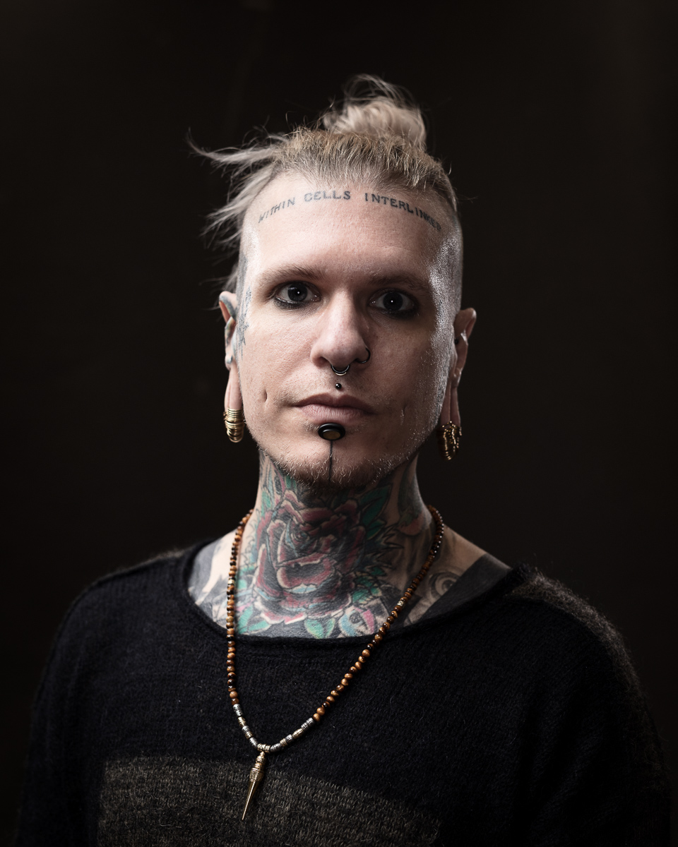 Person with tattoos and piercings facing camera solemnly.