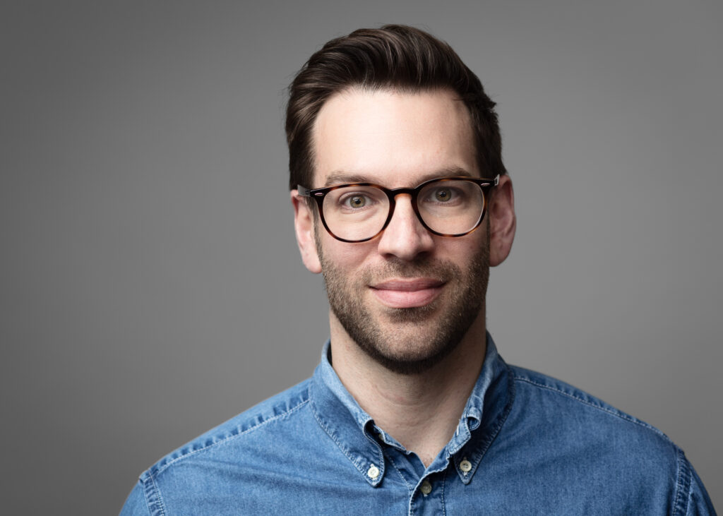 Smiling man with glasses and denim shirt
