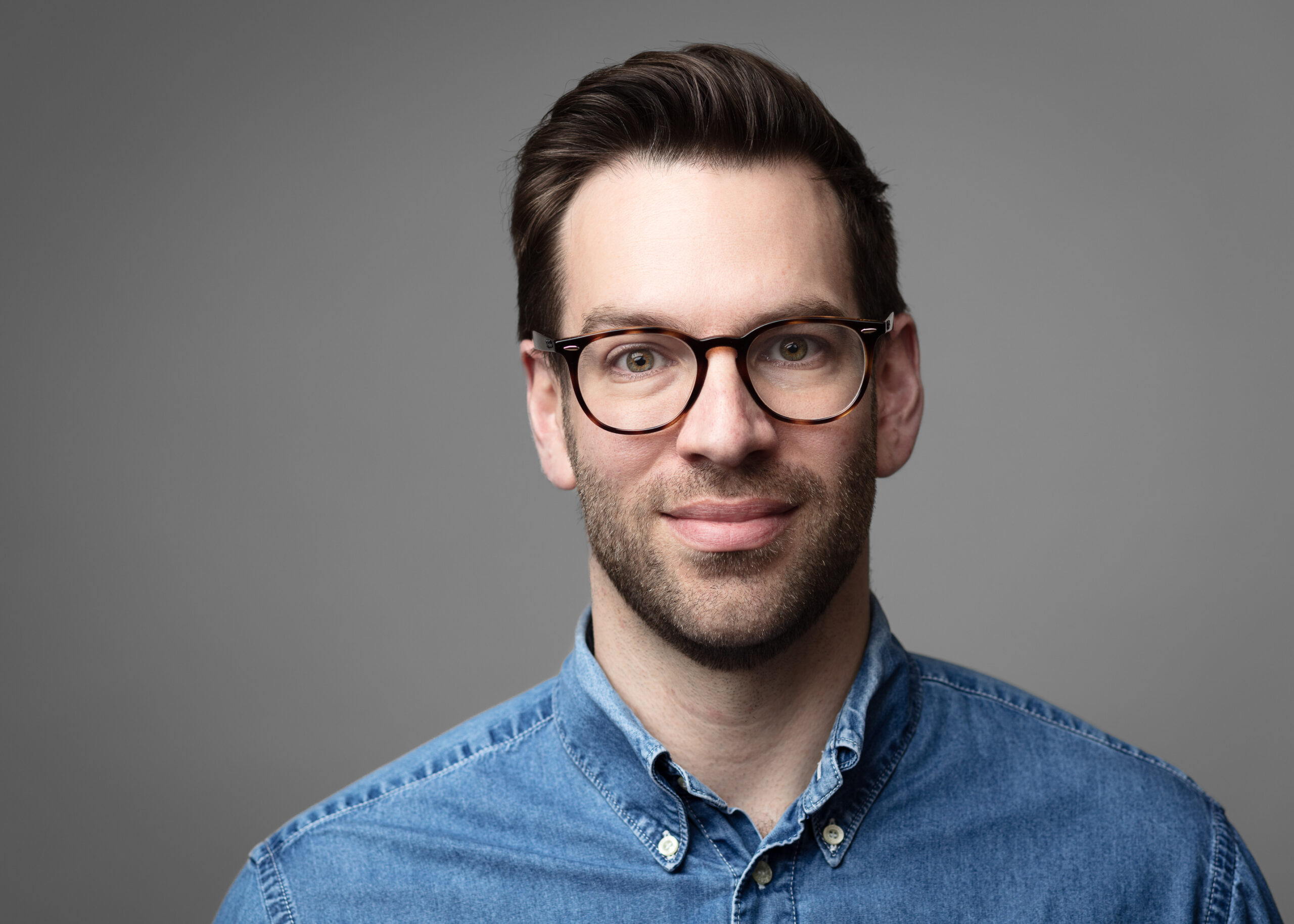 Smiling man with glasses and denim shirt