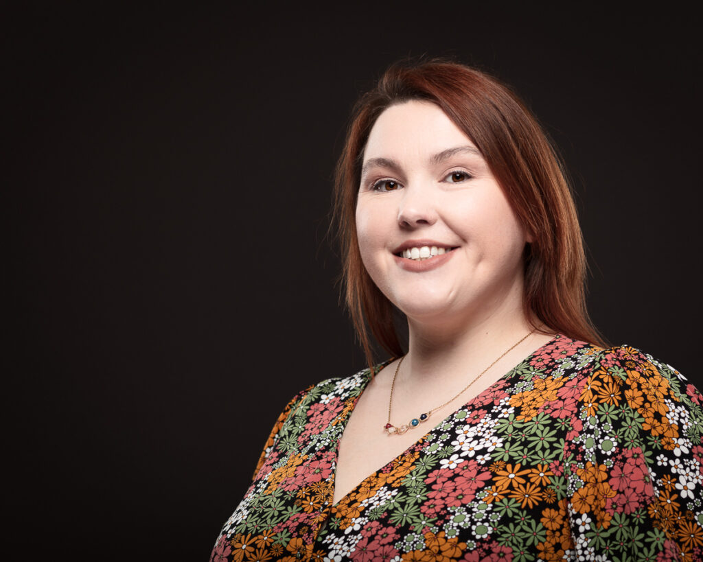 Smiling person in floral dress on dark background.