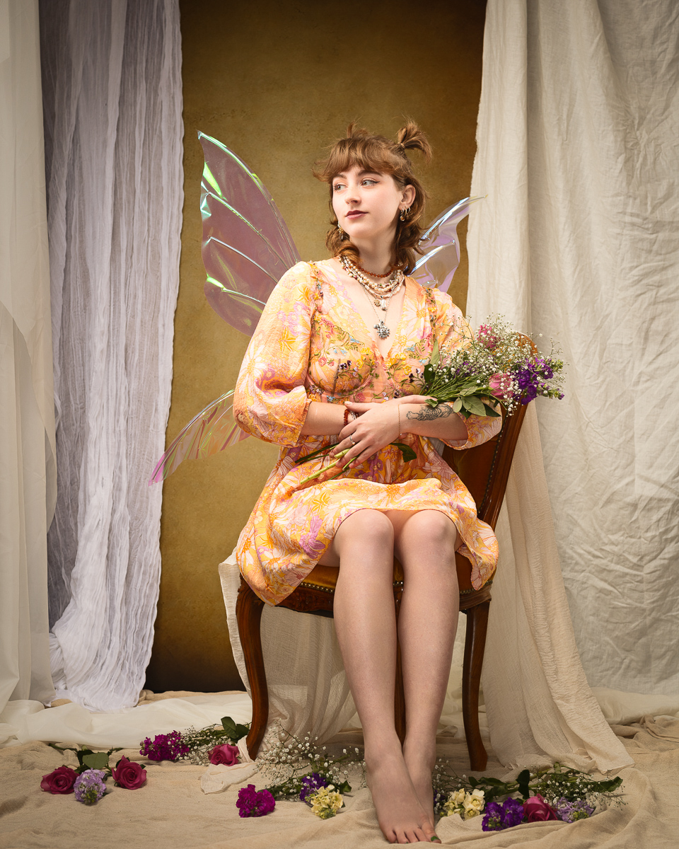 Woman with fairy wings holding flowers seated gracefully.