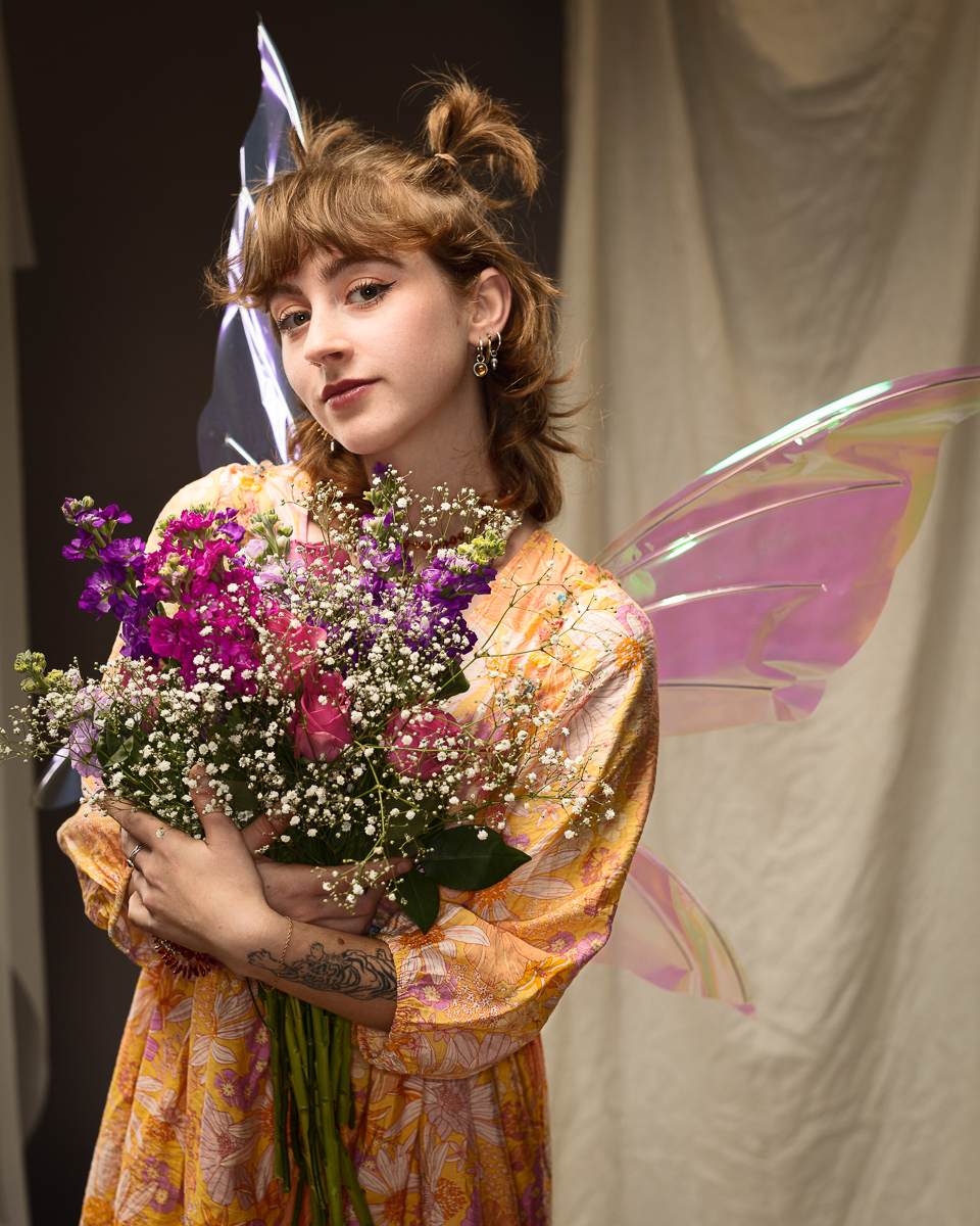 Person holding flowers wearing pink translucent fairy wings.