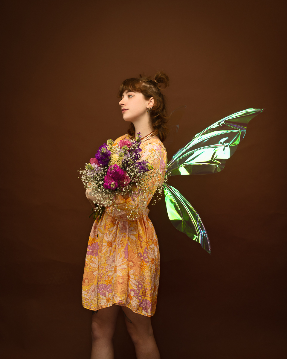Person with fairy wings holding flowers, orange dress